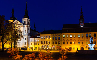 Fototapeta na wymiar View of illuminated central square of Czech city of Jihlava overlooking medieval cathedral, steeple of Town Hall and Neptune Fountain at dusk
