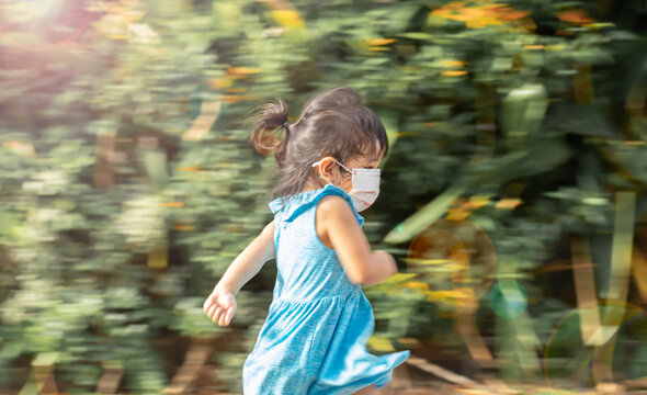 Blurry motion image of a girl kid wearing a medical mask having fun running as the outside activity has a blurred background.