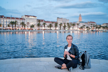 Fototapeta na wymiar Enjoying drink. Young woman drinking coffee on sea promenade.