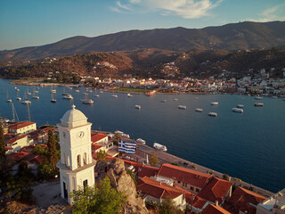 Drone view of Poros island. Clock tower in old town with traditional white houses near the sea....