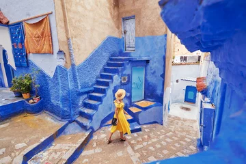 Deurstickers Kleurrijk reizen door Marokko. Jonge vrouw in gele jurk wandelen in de medina van de blauwe stad Chefchaouen. © luengo_ua