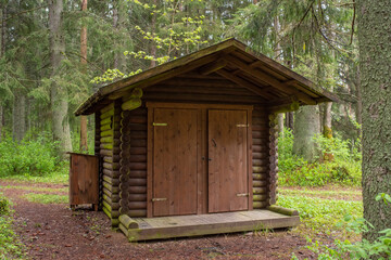Fototapeta na wymiar Wooden public toilet in the Estonian forest near the public rest and barbeque RMK area on a cloudy summer day.