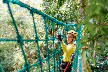 Young woman with climbing gear in an adventure extreme park climbing or passing on the rope road.