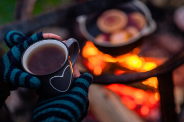 Obraz na płótnie Canvas Woman holds cup of the hot tea over a bonfire at night