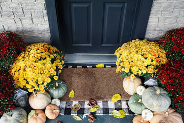 Welcome door mat of front porch that has been decorated for autumn with heirloom white, orange and...