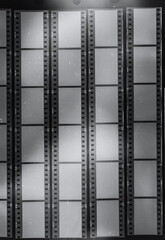 long empty 35mm film strips behind protection foil on black background, black and white film material with blank windows.