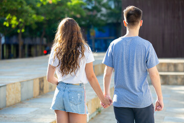 Guy and the girl go hand in hand. Back view