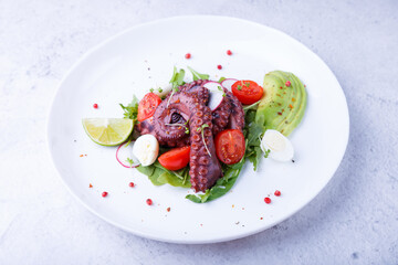 Warm salad with octopus, cherry tomatoes, avocado, arugula, quail eggs, radish and lime on a white plate. Traditional Mediterranean dish. Close-up, white background.