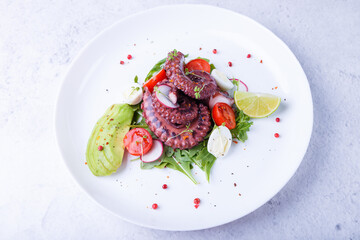 Warm salad with octopus, cherry tomatoes, avocado, arugula, quail eggs, radish and lime on a white plate. Traditional Mediterranean dish. Close-up, white background.