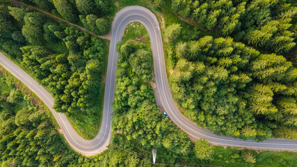 Obraz premium Aerial view of countryside road passing through the green forrest and mountain. Green pine and fir trees forest. Beautiful mountain road.