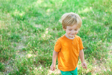 little blond boy smiling and walking on green grass in summer
