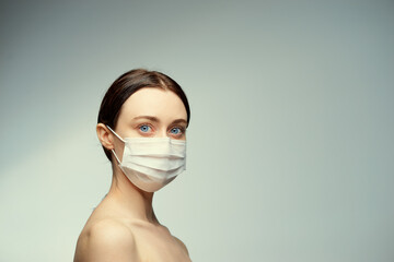 Portrait of a young beautiful woman in a medical mask on a white grey background.
