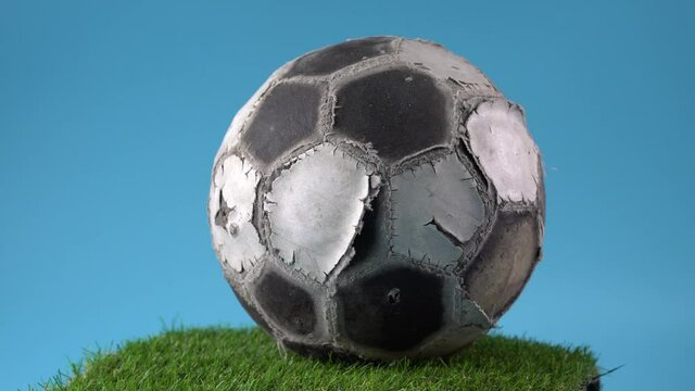Damaged football rotated on the turntable with green artificial grass and blue background
