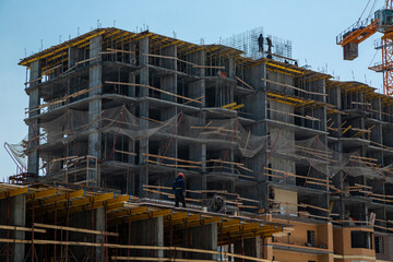 Two builders in helmets stand at the edge of a house under construction, construction site.