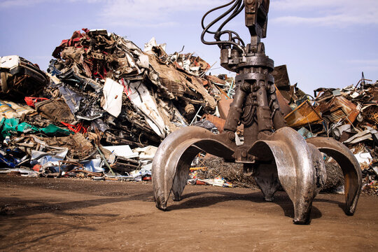 Metal junk yard with hydraulic lifting machine with claw attachment for scrap metal recycling.