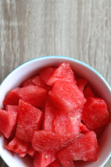 Bowl of watermelon cubes on wooden table. Flat lay.