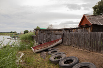 An old wooden boat sits on the shore next to an old house on the lake.
