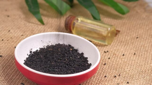 Black Cumin drops in a container with oil in a jar on table.