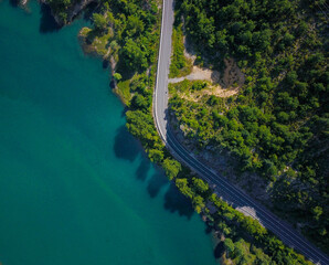 Aerial view of a tropical road surrounded by trees and a blue lake from above by a drone.