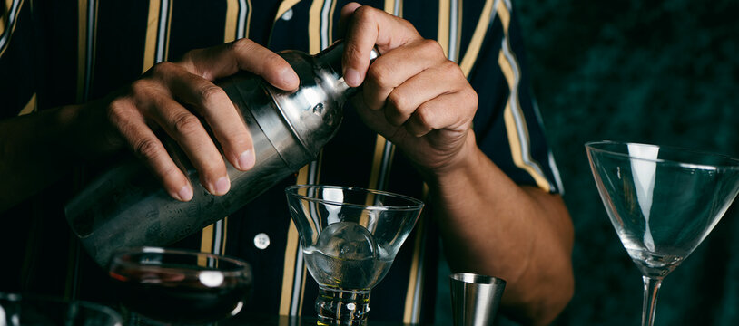man prepares a cocktail in a metal shaker, web banner