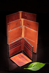 Group of leather wallets and a green leaf on a dark background.