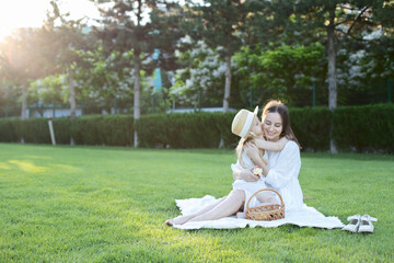 Mother and daughter sit in a clearing on a blanket in the park.