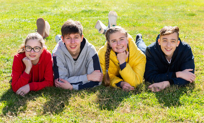 Group of smiling teenage boys and girls having fun together on spring day, lying on green grass