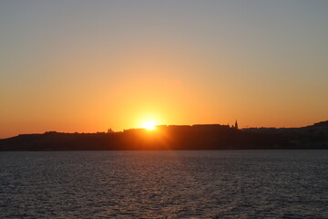 Naklejka na ściany i meble Maltese sunset from mediterranean sea, view on Gozo island from parome boat, way back home