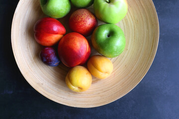 Wooden bowl with various fruit on dark background. Flat lay.