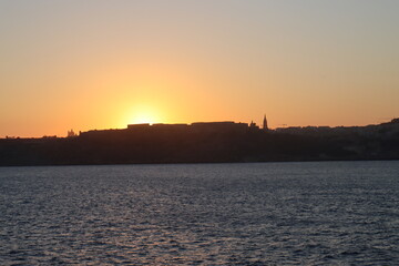 Fototapeta na wymiar Maltese sunset from mediterranean sea, view on Gozo island from parome boat, way back home