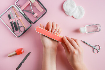Woman does a manicure at home. Hands with a nail file on pink background.