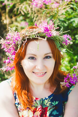 Portrait of young beautiful red-haired woman with  wreath of pink flowers on her head. Attractive lady smiles. Summer style