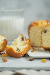 Homemade freshly baked butter sponge cake with raisins on white table with glass of milk. Sweet bakery - beautiful breakfast, macro shot, close up view with copy space. Biscuit dessert.