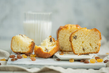 Homemade freshly baked butter sponge cake with raisins on white table with glass of milk. Sweet bakery - beautiful breakfast, macro shot, close up view with copy space. Biscuit dessert.