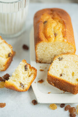 Homemade freshly baked butter sponge cake with raisins on white table with glass of milk. Sweet bakery - beautiful breakfast, macro shot, close up view with copy space. Biscuit dessert.