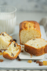 Homemade freshly baked butter sponge cake with raisins on white table with glass of milk. Sweet bakery - beautiful breakfast, macro shot, close up view with copy space. Biscuit dessert.