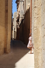 Fototapeta na wymiar Woman in long dress walking old town of Valletta, sands and ruins tiny square streets
