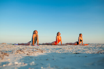 young women doing yoga on the seashore in the summer