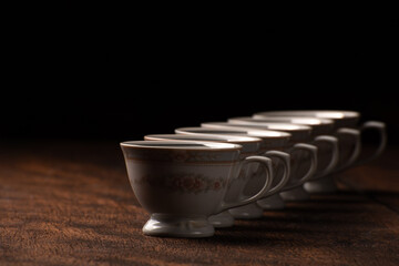 Porcelain cups, beautiful porcelain cups geometrically arranged on rustic wood, dark background, selective focus.