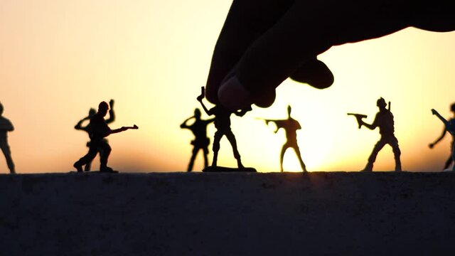 Silhouette shot of hand of kid placing toy soldiers in front of the sunset	