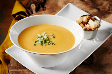 Pumpkin cream soup in white beautiful plate on wooden cut on a metal rusty background. Photo for the menu and site. Space for text. High quality photo