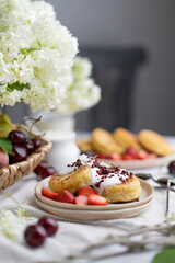 Cottage cheese fritters (ricotta pancakes or syrniki) with sour cream (yogurt) on white table with berries and flowers. Healthy calcium breakfast Traditional russian food. Country rustic style