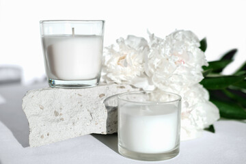 white scented soy wax candles on a natural stone and peony flowers. floral fragrance for cozy home. aromatherapy and wellness concept