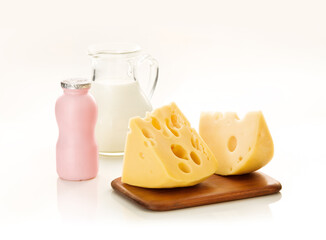 Pedaço de queijo, iogurte e jarra de leite no fundo branco.