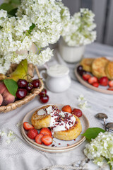 Cottage cheese fritters (ricotta pancakes or syrniki) with sour cream (yogurt) on white table with berries and flowers. Healthy calcium breakfast Traditional russian food. Country rustic style