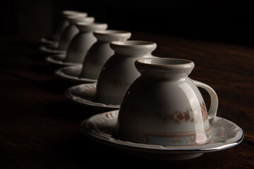Porcelain cups, beautiful porcelain cups geometrically arranged on rustic wood, dark background, selective focus.
