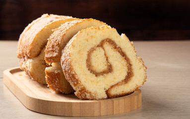 Rocambole, Sliced ​​rocambole stuffed with dulce de leche on a wooden tray on a table. dark background, selective focus.