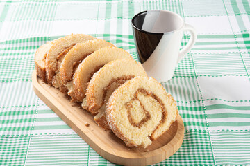 Rocambole, Sliced ​​roacambole stuffed with dulce de leche on a wooden tray and a cup on a table with a checkered tablecloth. dark background, selective focus.