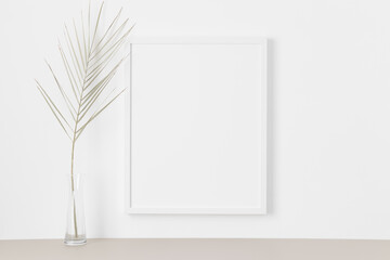White frame mockup on the wall with a palm leaf.