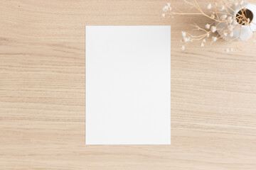 White invitation card mockup with a gypsophila on the wooden table. 5x7 ratio, similar to A6, A5.